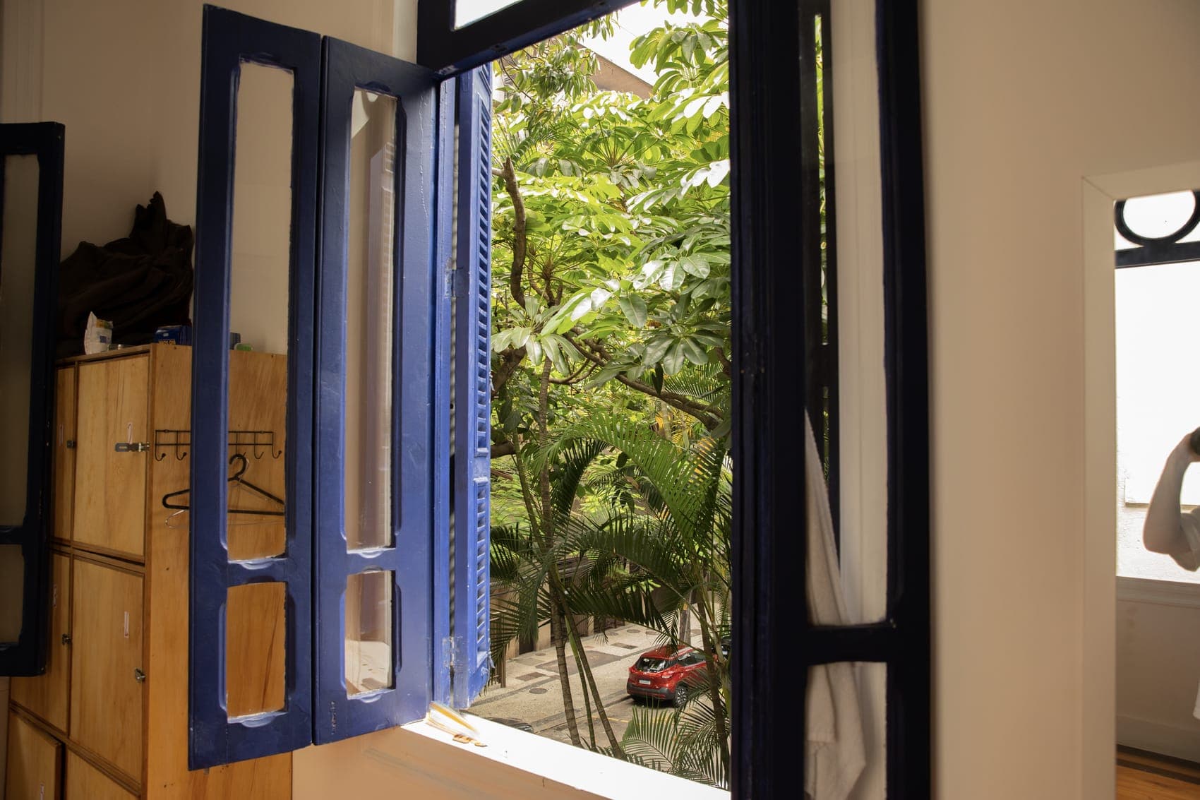 Blue-shuttered window and wooden lockers looking onto Humaitá's trees